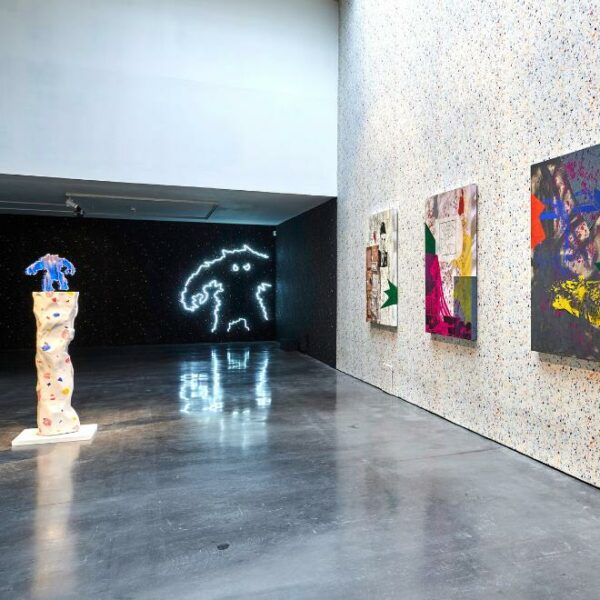 A photograph of an exhibition space in the New Art Exchange, featuring three paintings, a sculpture and a neon sign.