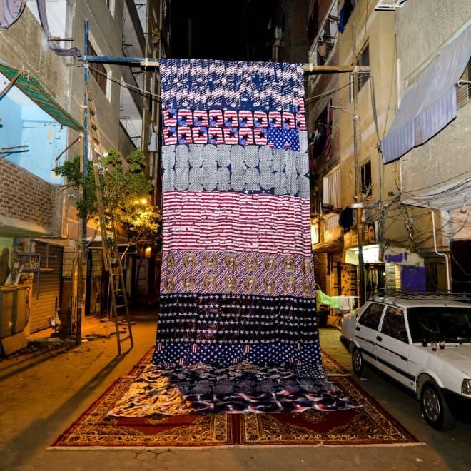 A photograph of a large patterned cloth hanging from pillars on a building.