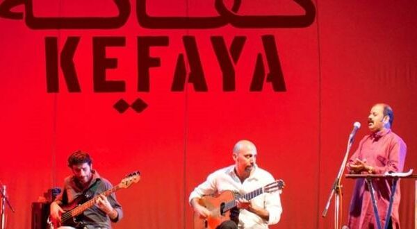 A photograph of the band Kefaya performing, the group features three members, two on guitars and a singer.