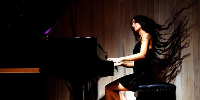A photograph of Zoe Rahman performing, she plays the piano while her long hair flows in the wind