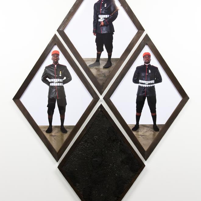 A photograph of artwork by Leo Asemota at the New Art Exchange, depicting 4 diamond frames which form a larger diamond, three of the diamonds have pictures of men inside them wearing black uniforms and orange hats