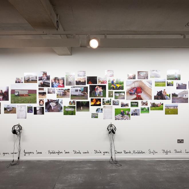A photograph of an exhibition wall at the New Art Exchange featuring a collage of images stuck to the wall and headphones mounted onto it.