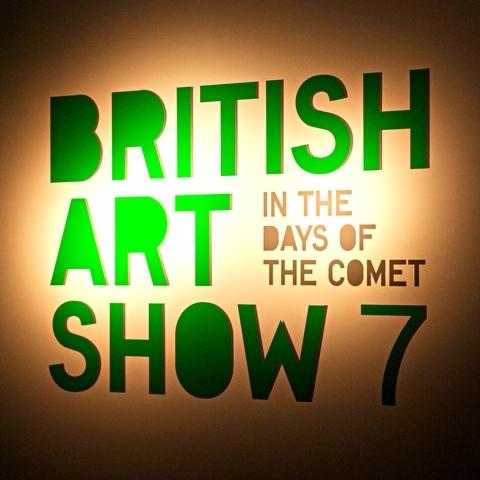 A photograph of a wall with a spotlight on it with green text which reads "British Art Show 7 In the Days of the Comet"