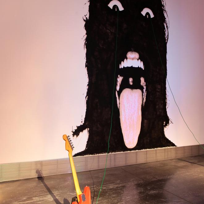 A photograph of a wall with an art piece on it depicting a black silhouette with their tongue out and white eyes.
