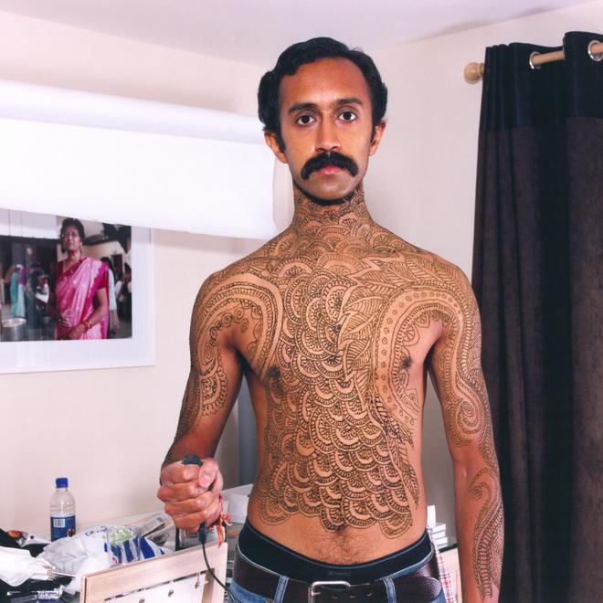 A photograph of a man from the waist up with his shirt off covered in henna