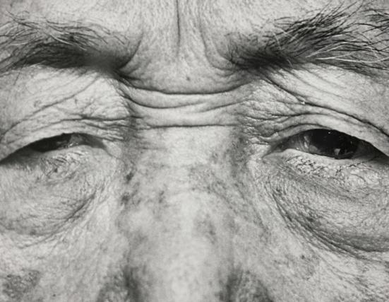 An up-close photograph of an elderly man's eyes with long eyebrow hairs above them