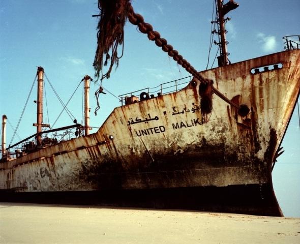 A photograph of a rusting old ship on a sandy shore with the words 'United Malik' written on it.