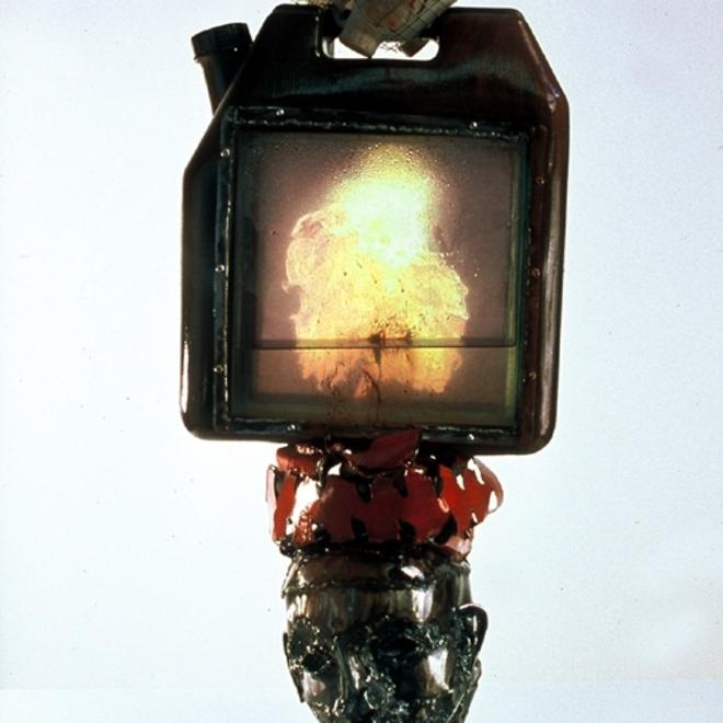 A photograph of a gas canister on a podium, there is a translucent panel in the middle of the canister with a fire inside of it.