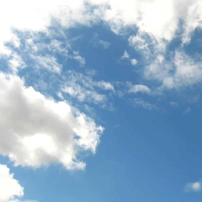 A photograph of blue skies and sun shining behind clouds.