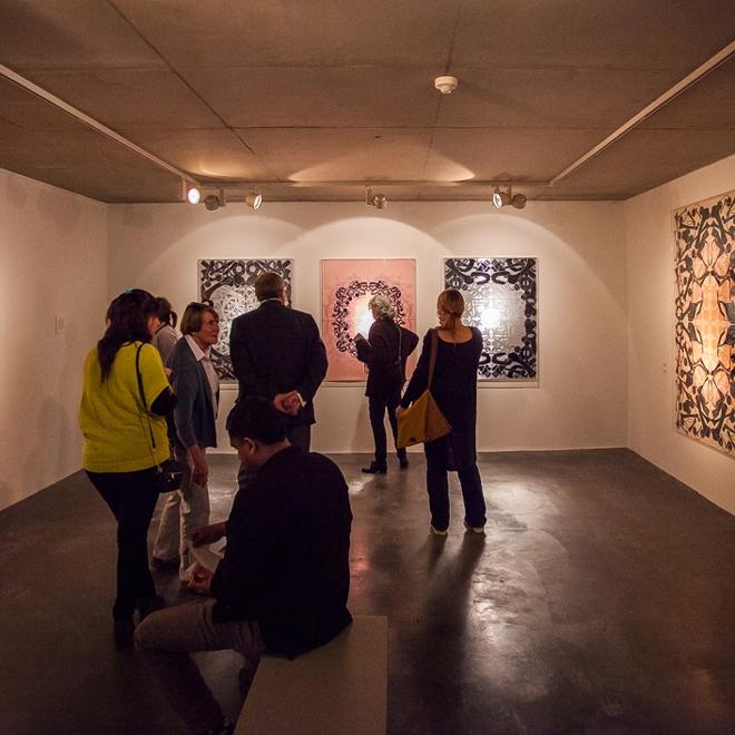 A photograph of a group of people looking at an hung up artwork at an exhibition.
